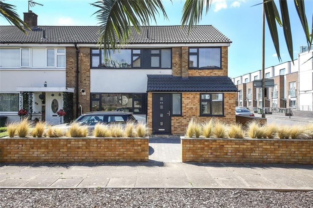 Renovated semi-detached house with black front door, large windows, and ornamental grasses in brick planters, in a suburban street.