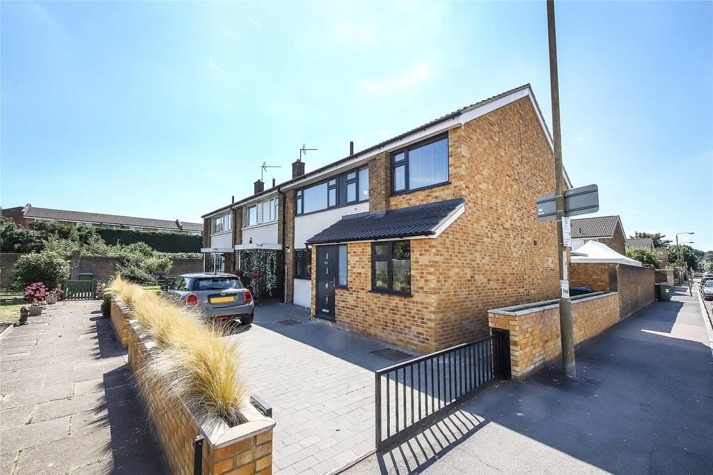 Corner house with a double-storey side extension, featuring brick walls and driveway parking, under a clear blue sky.