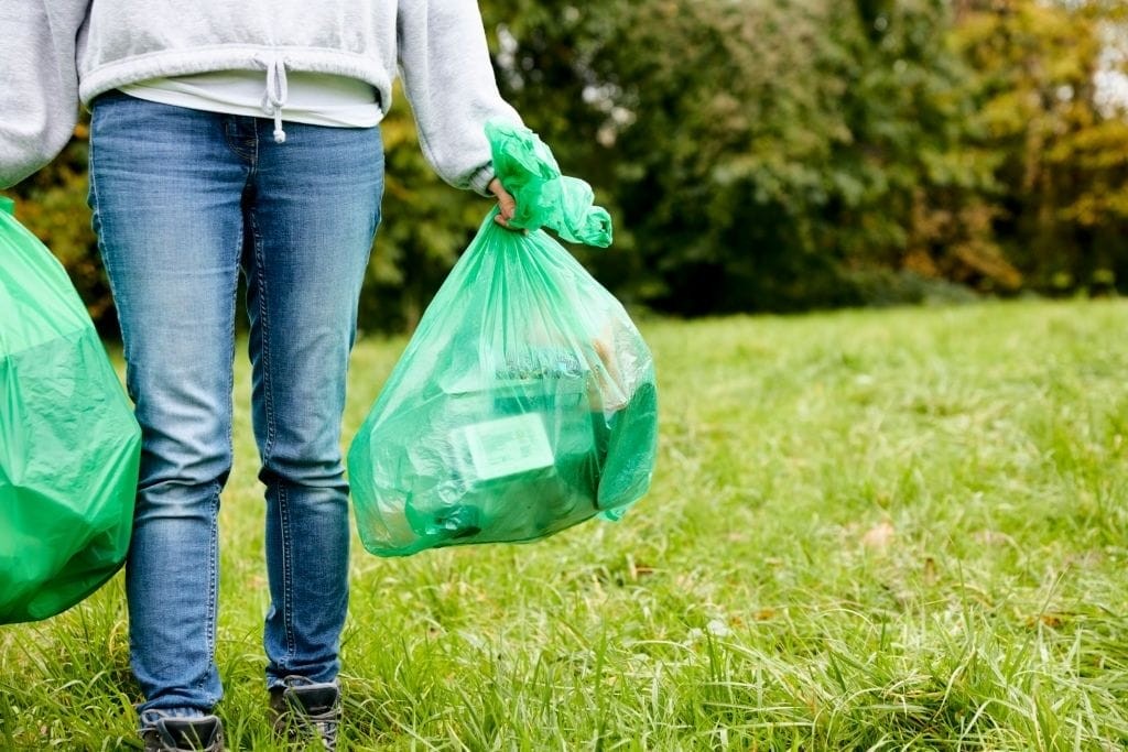 Person participating in environmental cleanup holding green garbage bags, illustrating community involvement in sustainable practices and waste management in green outdoor spaces.
