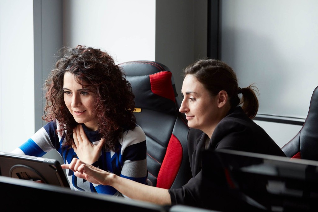 Two professional female architectural designers collaborating and discussing work on a computer in a modern office setting, focusing on teamwork and technology in the workplace.