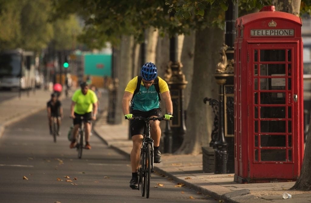 Cyclists riding on city street with iconic red British telephone box, promoting urban cycling and sustainable transportation in London, UK.