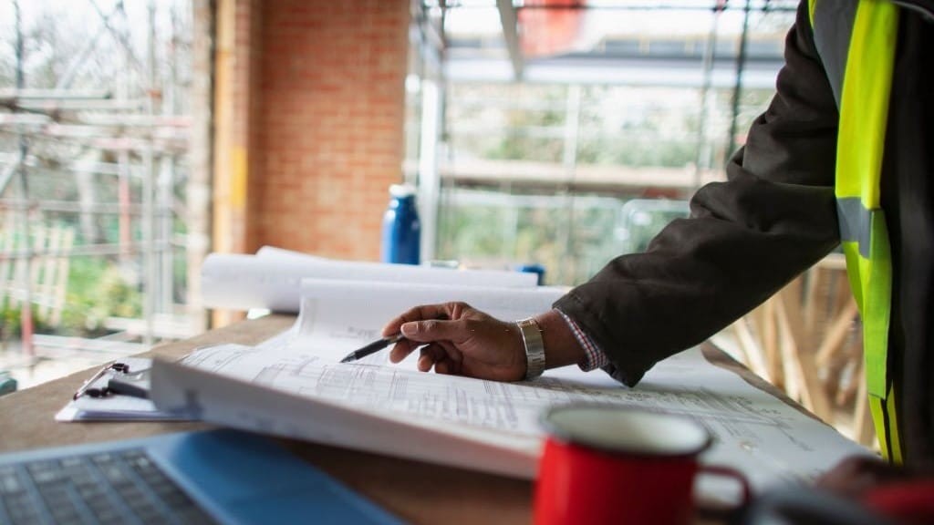 Construction project manager reviewing blueprints on a worktable at a construction site with scaffolding in the background.