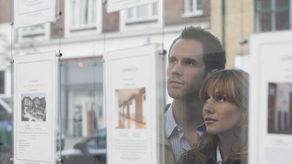 A couple looks through an estate agent's window at property listings, possibly considering homes where the four-year rule or ten-year rule might apply to planning permissions.