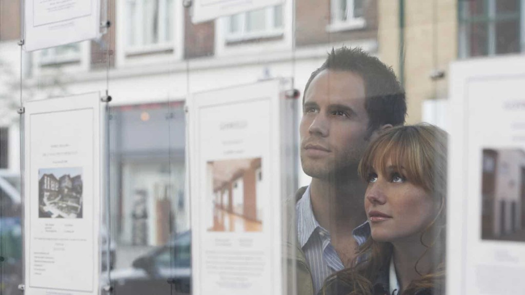 Prospective homebuyers intently viewing real estate listings in a property agent's window, reflecting their search for a new home in an urban neighborhood.