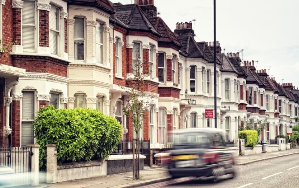 Classic Victorian terraced houses lining a quiet street in the UK with a blurred car passing by, showcasing traditional British architecture and urban design.