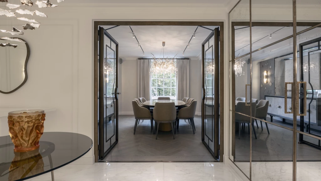 Grand entrance hall of a turnkey super home, defined by mirrored walls and steel-framed glass doors leading into a chandelier-lit dining room.