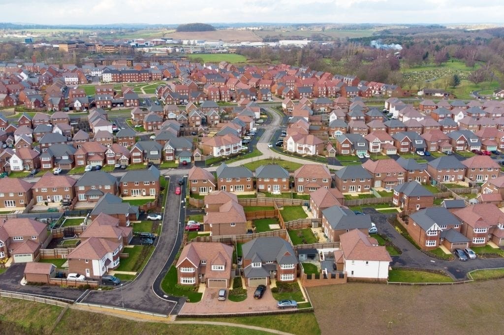 Overhead view of a modern British housing estate with uniform red-roofed houses, neat gardens, and winding streets, showcasing typical suburban development in the UK.