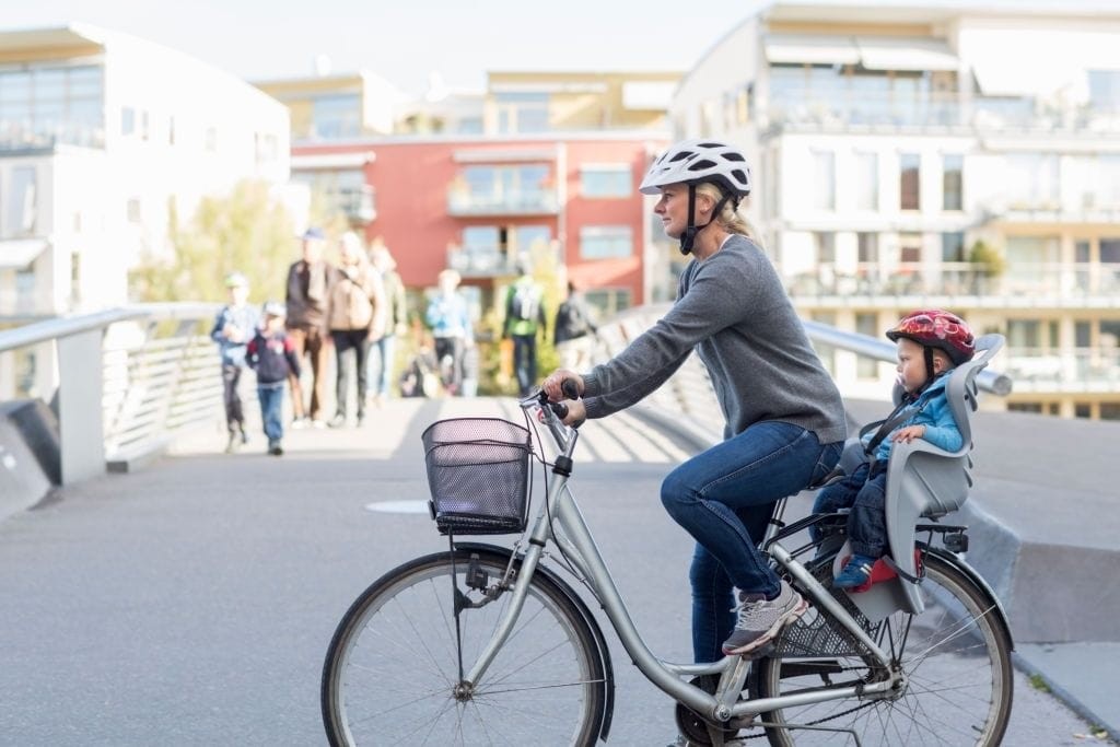 Mother and child enjoying a bike ride in a vibrant urban neighbourhood, promoting active lifestyle and sustainable transportation in well-planned city areas.