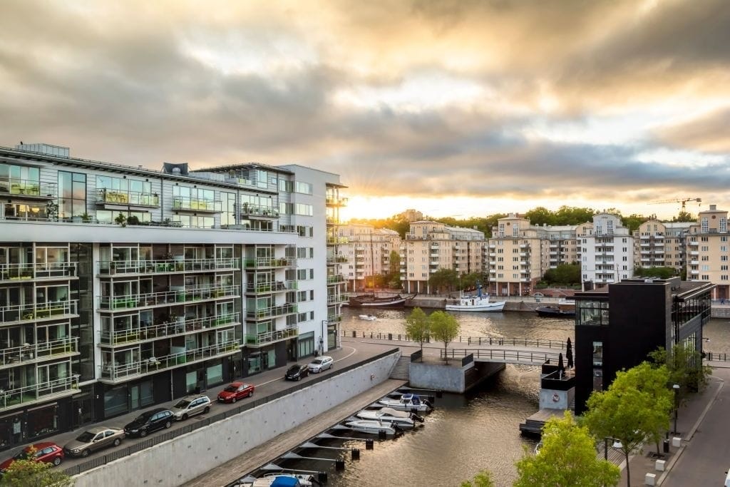 Sunset view of a modern waterfront residential complex with contemporary architecture, showcasing glass facades and balconies overlooking a canal and marina in an urban neighbourhood.