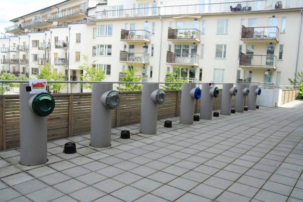 Sustainable waste management system featuring recycling and trash disposal units in front of modern apartment buildings, illustrating urban planning focused on cleanliness and environmental responsibility.