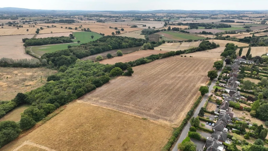 Aerial view of agricultural land and countryside on the edge of a residential settlement, illustrating the debate around Grey Belt reform and land release for housing development in England.