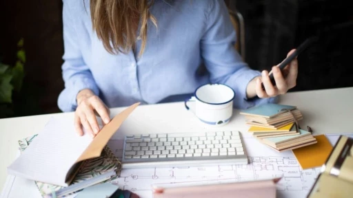 Homeowner reviewing planning documents and architectural floor plans at a desk while using a smartphone, illustrating how AI-assisted planning applications, digital planning tools and online planning permission processes can support residential development projects.
