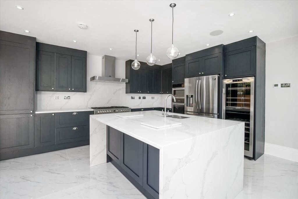 Sleek and modern kitchen interior with charcoal gray cabinets, marble countertops, and a central island, complemented by glass pendant lighting and high-end stainless-steel appliances, reflecting a minimalist and sophisticated design aesthetic.