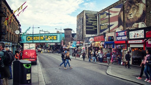 Two people crossing Camden High Street with the well-known Camden Lock railway track in the background