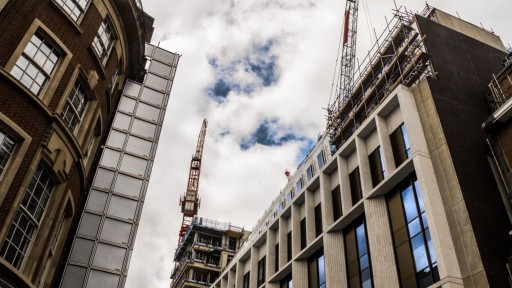 Photograph taken from street view in Camden, looking up to a cloudy sky and to the ongoing upward construction happening in the area