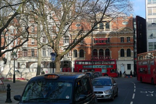 Street view of London's red double decker buses and black taxi cabs driving around Sloane square and in front of the Royal Court Theatre