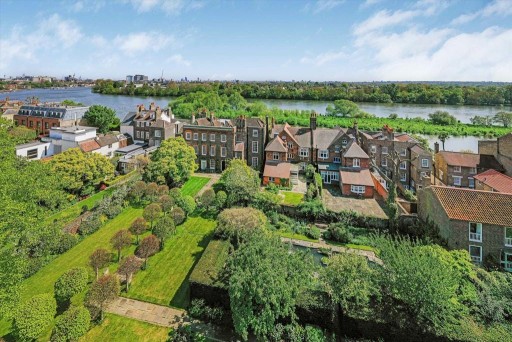 Scenic aerial view of Chiswick neighborhood with rows of traditional British houses, lush private gardens, and the expansive River Thames in the background under a clear blue sky.