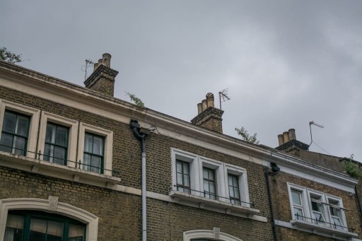 Exterior view of the top floor to three terrace houses and their sash windows london made from timber in various frame shapes and colours such as peach, forest green, brown and white