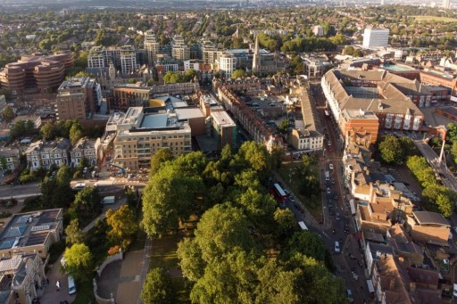 Aerial view of Ealing, London, with a blend of modern and traditional buildings amidst greenery, showcasing the area's unique urban landscape and bustling streets.