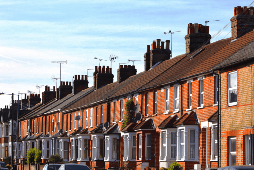 Diagonal perspective of a row of traditional red-brick terraced houses in Ealing with characteristic chimneys and satellite dishes under a clear blue sky.