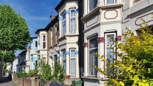 Row of traditional terrace houses in East London with small front yards and triple glass bay windows with various coloured Victorian pilaster capitals creating a clear separation for each dwellings 