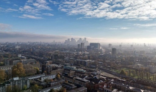 Aerial view of the East London skyline on a blue and slightly cloudy day with lowrise buildings at the front of the photograph and high rise buidings of the city of London in the far back of the skyline