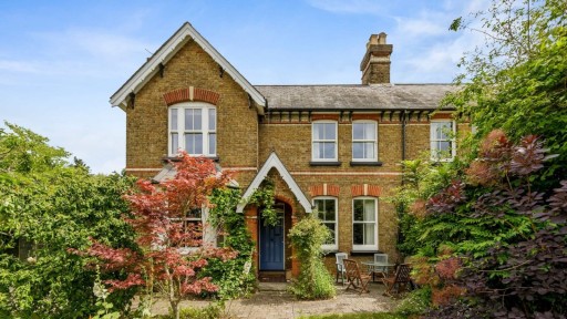 Traditional brick Victorian house in Guildford with gabled roofing, blue front door, and a lush front garden featuring a variety of green and red foliage.