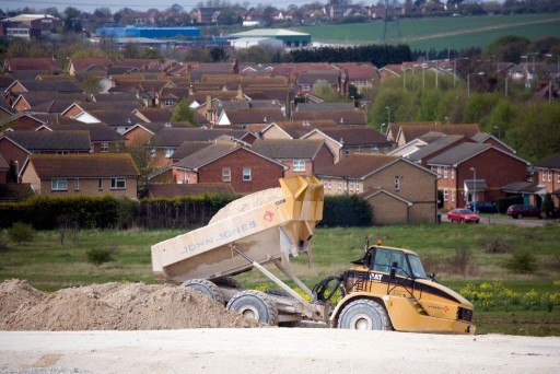 Drump truck backing soil onto a construction site with a background of development neighbourhoods