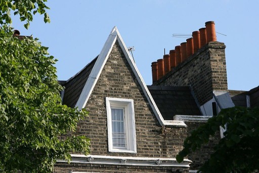 Pitched roof with contrast of dark brown brickwork and white trimmings not only on the roof but also around a narrow tall window on the top floor