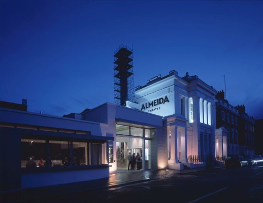 Night photo of the lit up Almeida Theatre in Islington, London with blurred visitors at the front entrance