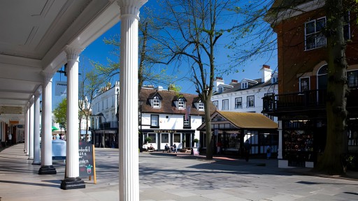 Quaint and bustling town square in Kent, England, showcasing historic architecture with white-painted facades and gabled rooftops, framed by elegant Doric columns and vibrant blue skies, embodying the classic British charm.