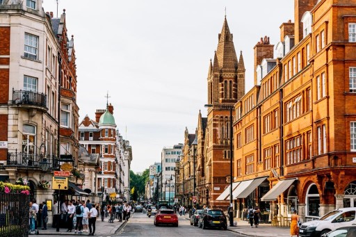 Vibrant photograph of a busy high street with Mayfair with sidewalks filled with pedestrians and cars parked on the sides as well as moving forward