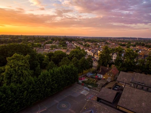 Aerial view of the sun set on a lovely and quaint residential neighbourhood with rows of semi-detached and terrace houses with plenty of green back gardens for each family home as well as the local primary school with a large and secure backyard playground