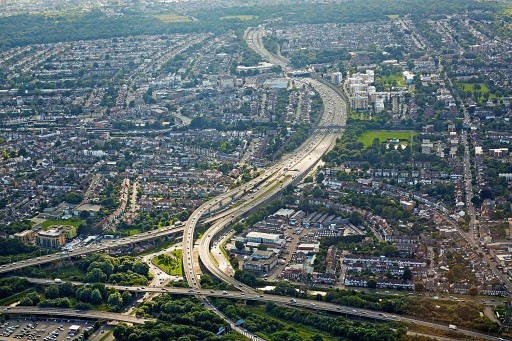 Aerial view on a slightly cloudy and sunny day of a highly condensed residential neighbourhood on the left hand side of a large winding motorway and industrial zones on the bottom right side of the highly used motorway