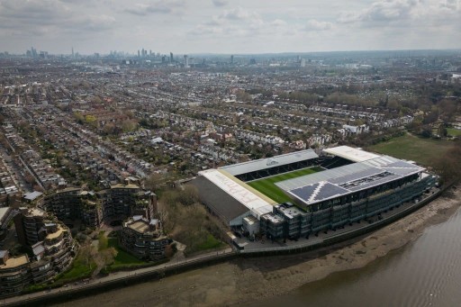 Aerial view from the Thames river of the Premier League football stadium and rooftop views of the city's flatted developments and housing with skycrapers peeking through at the back of the skyline