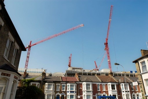 Amongst streets of terraced houses in West London is the upward view of four tall red cranes working two to three streets away on the latest flatted development