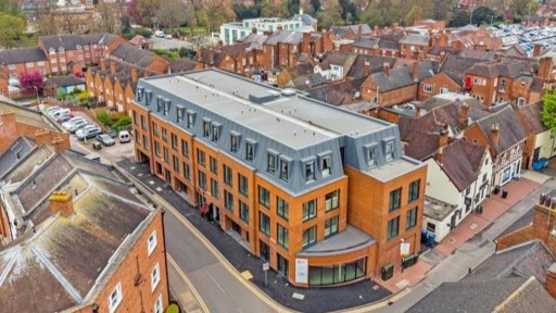 Aerial view of a new modern mixed-use development in West Midlands with brick facade, contrasting with the surrounding traditional terraced housing and commercial buildings, reflecting current real estate trends and urban regeneration efforts.