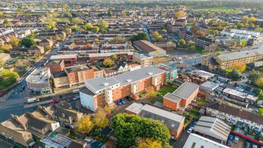 Aerial view of a bustling Wimbledon neighborhood, showcasing a mix of residential housing, apartment buildings, and commercial properties amid the changing autumn foliage.