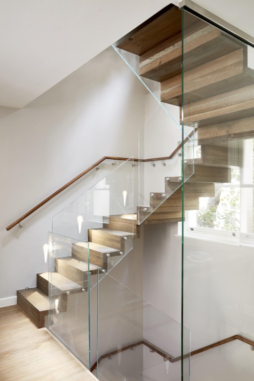 White stairwell with natural wood floating staircase with a matching natural wood handrail and clear glass railing.