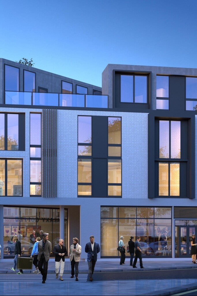 Contemporary new-build flats in London at dusk, featuring modern architectural design with large glass windows and a mix of white brick and dark grey exterior. The vibrant urban development includes ground-floor retail spaces and stylish residential units, ideal for city living. Pedestrians and shoppers add to the lively street atmosphere.