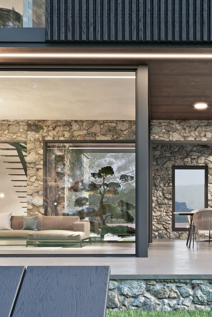 Floor to ceiling windowed lounging area leading directly onto a concreate open patio with decorative stone walls on the inner part of the room blending out to the exterior