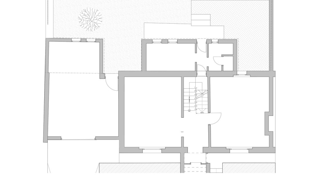 Architectural floor plan drawing of the existing lower ground floor, showing detailed room layouts, walls, and door placements, with a textured representation of flooring areas and a schematic tree indicating an outdoor space, for use in building design and construction documentation.