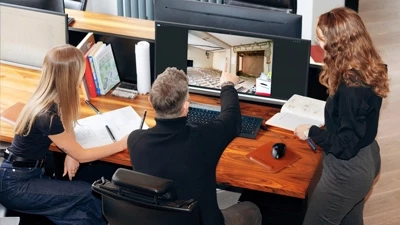 Team of architectural designers, interior designers, graphic designer and planning consultants around a shiny wooden table discussing Green Belt project with various designs printed and spread on the table as well as on the tv screen behind them